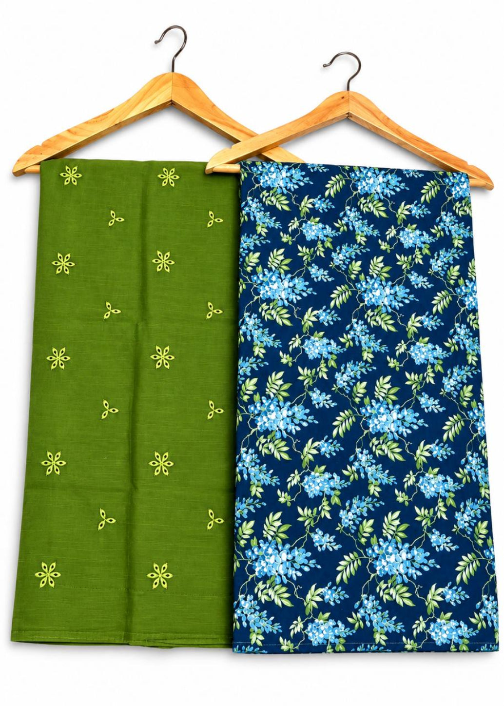 Two folded fabric garments hanging on wooden hangers against a white background. The left garment is olive green with small yellow embroidered motifs, and the right garment is navy blue with a light blue and yellow floral print.