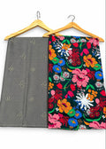 Two folded fabric garments hanging on wooden hangers against a plain white background. The left garment is solid gray with small metallic geometric motifs, and the right garment has a dense multicolor floral print on a dark background with pink, blue, orange, yellow, green, and white flowers.