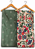 Two folded patterned fabrics hanging on wooden hangers against a white background. The left fabric is olive green with small white embroidered motifs.