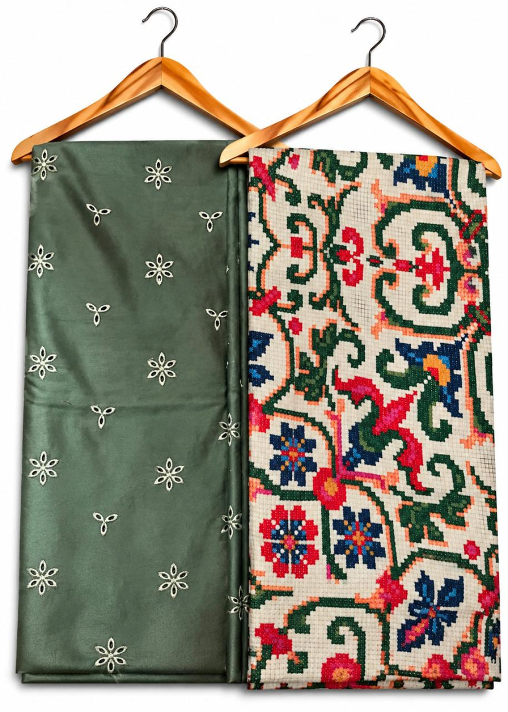 Two folded patterned fabrics hanging on wooden hangers against a white background. The left fabric is olive green with small white embroidered motifs.