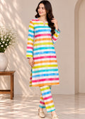 A woman modeling a long-sleeve kurta and matching pants set with vibrant, multicolored horizontal stripes in pink, blue, yellow, green, orange, and white, set against a warm beige interior background.