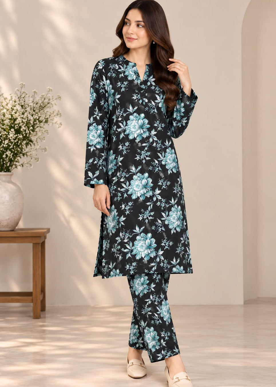 A woman modeling a black long kurta set with a light blue and white floral print, paired with matching pants, in a brightly lit indoor setting.