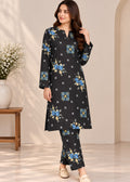 A woman modeling a black long kurta set with a blue and yellow floral print and small white star motifs, paired with matching pants, in a warm beige interior setting.