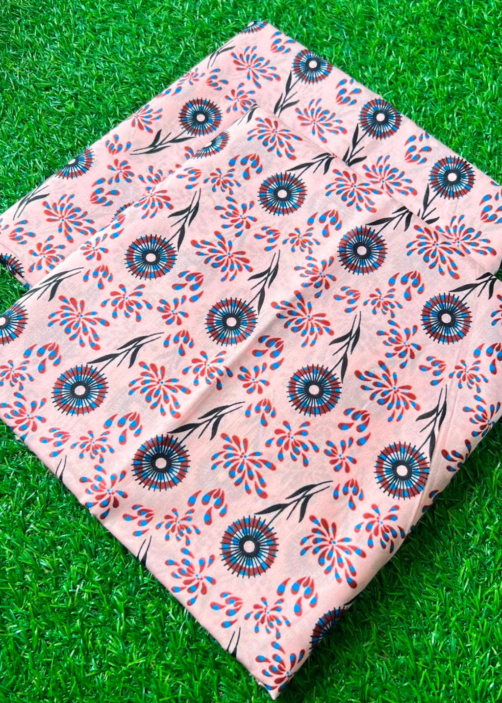 A folded piece of peach-colored fabric with a blue and red floral pattern, displayed on a green grass-like surface.