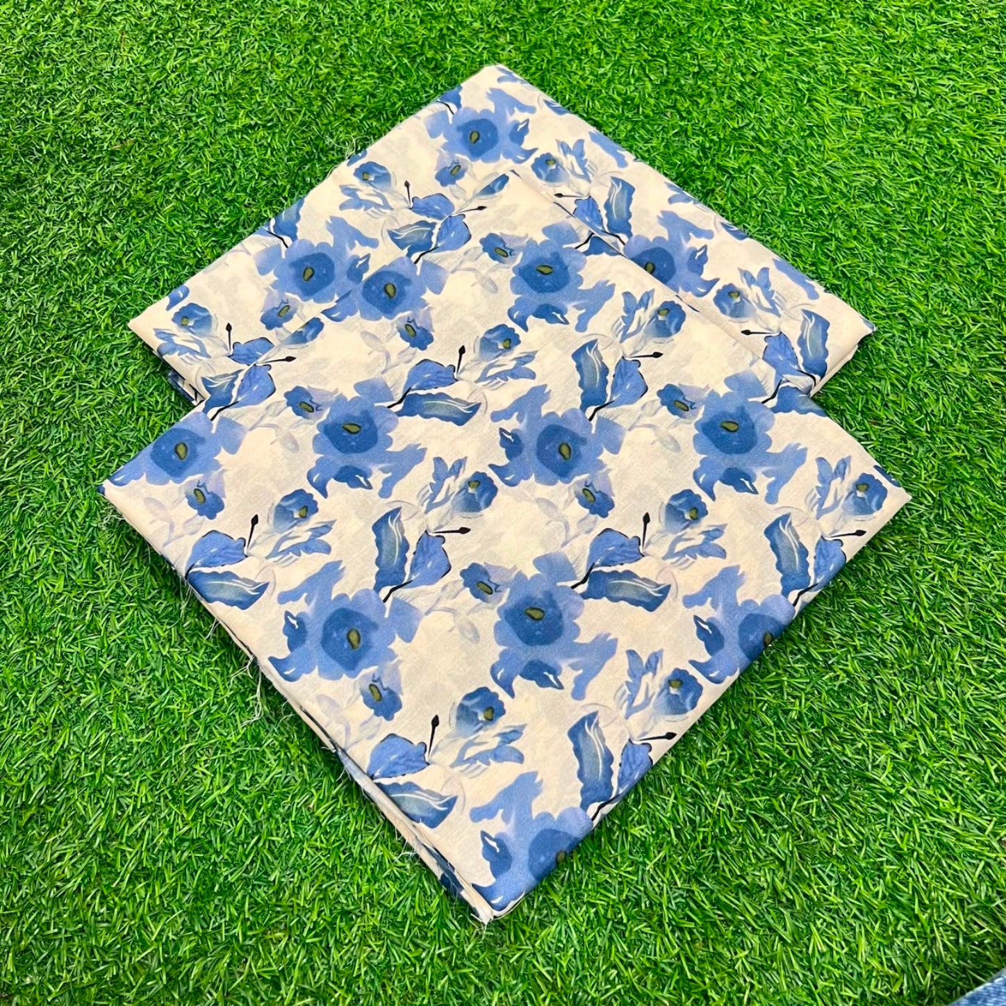 Two square fabric pieces with a blue floral pattern on a cream background, laid flat on green artificial grass.