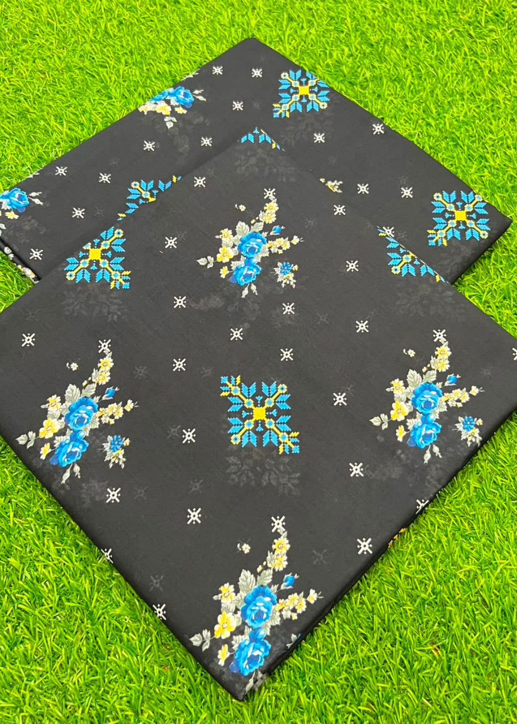 Two rectangular black mats with blue and yellow floral patterns and small white star-like motifs, laid on bright green grass.