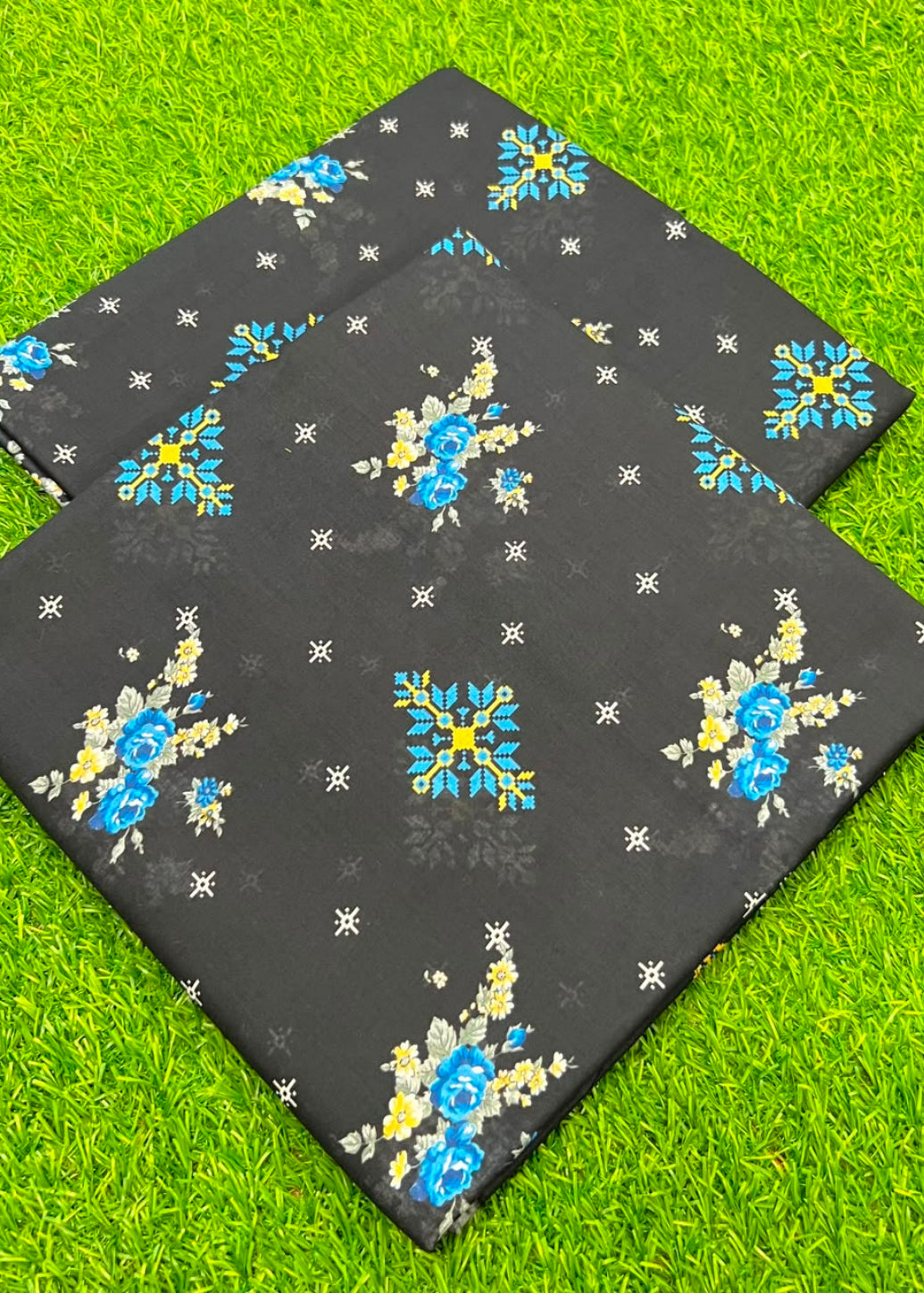 Two rectangular black mats with blue and yellow floral patterns and small white star-like motifs, laid on bright green grass.