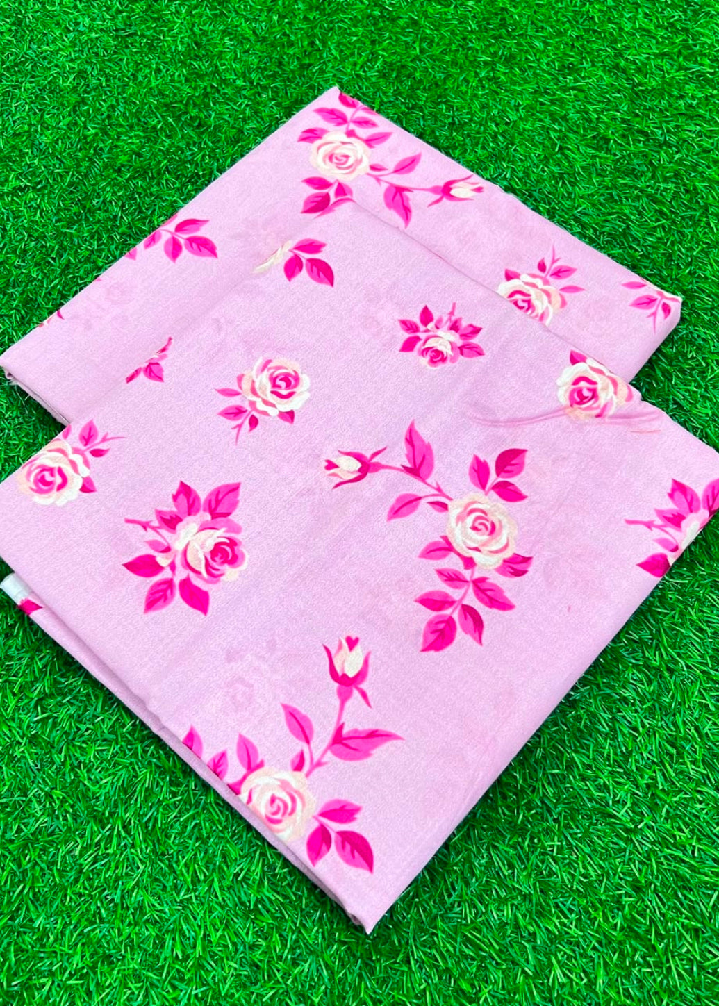 A folded light pink fabric with a pink and cream rose floral pattern, displayed on a green artificial grass background.