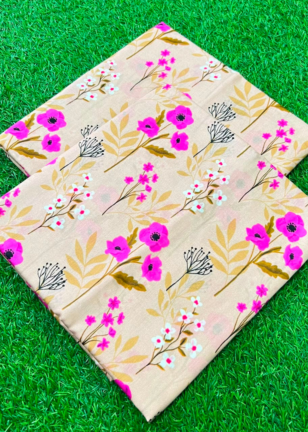 Two rectangular fabric pieces with a floral print in pink, green, and white on a beige background, laid flat on a green grass-like surface.