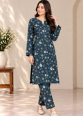 A woman modeling a dark teal blue floral printed kurta and trouser set in a warm, sunlit indoor setting with a wooden side table and white flowers in the background.