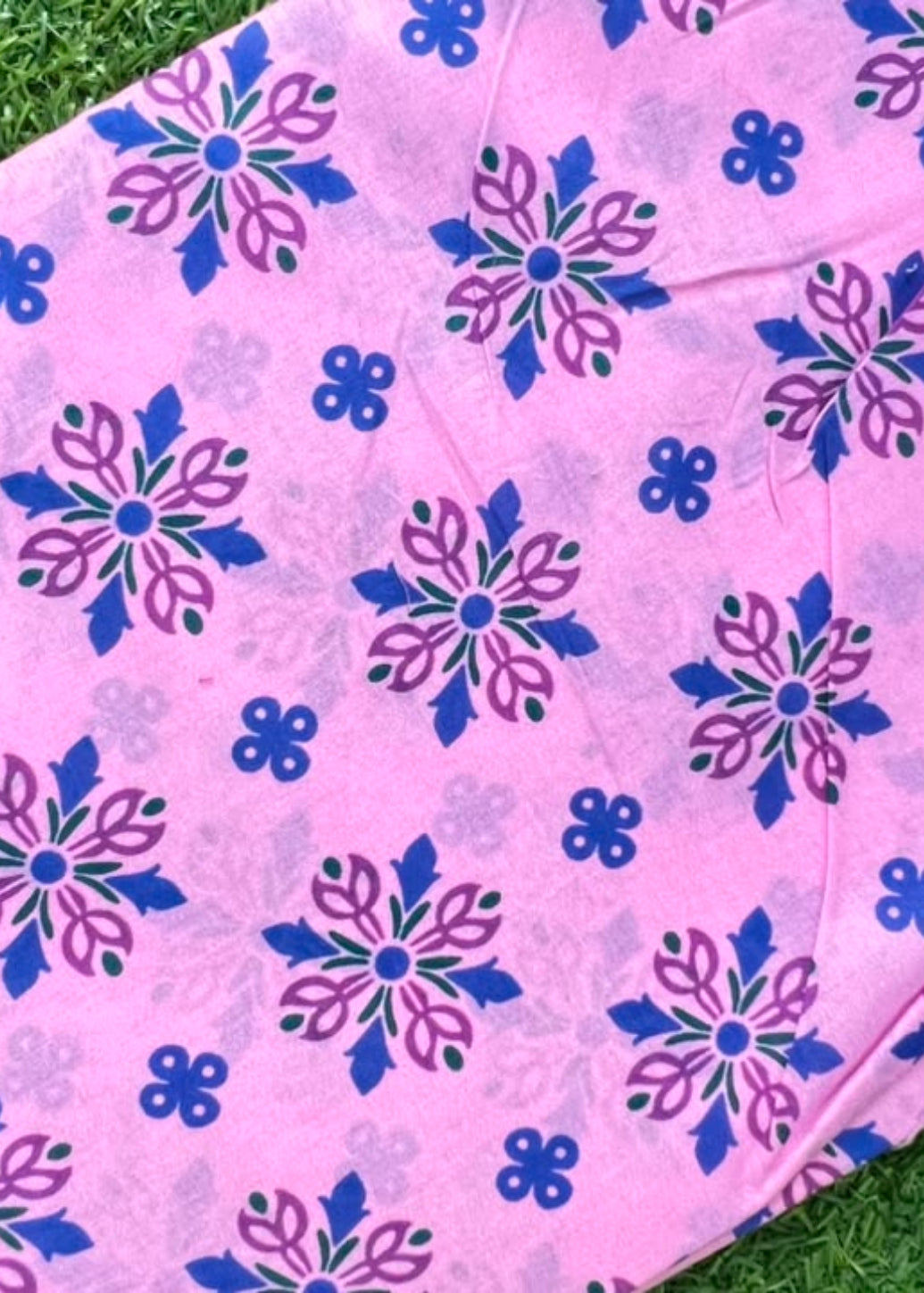 Pink fabric with a blue and purple floral pattern, laid flat on green grass.
