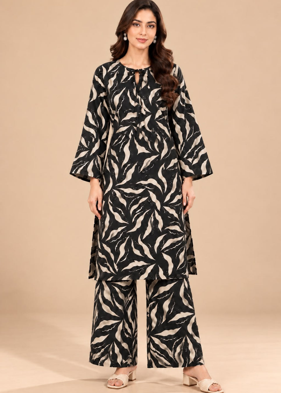 A woman modeling a black and beige abstract leaf-patterned kurta set with matching wide-leg pants, standing against a solid beige studio background.