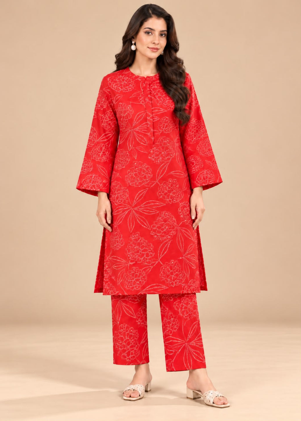 A woman modeling a red three-piece kurta set with a white floral pattern, consisting of a long-sleeve tunic, matching pants, and a dupatta, set against a solid beige studio background.