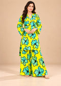 A woman modeling a bright yellow two-piece kurta set with a bold turquoise and black floral print, standing against a solid beige studio background.