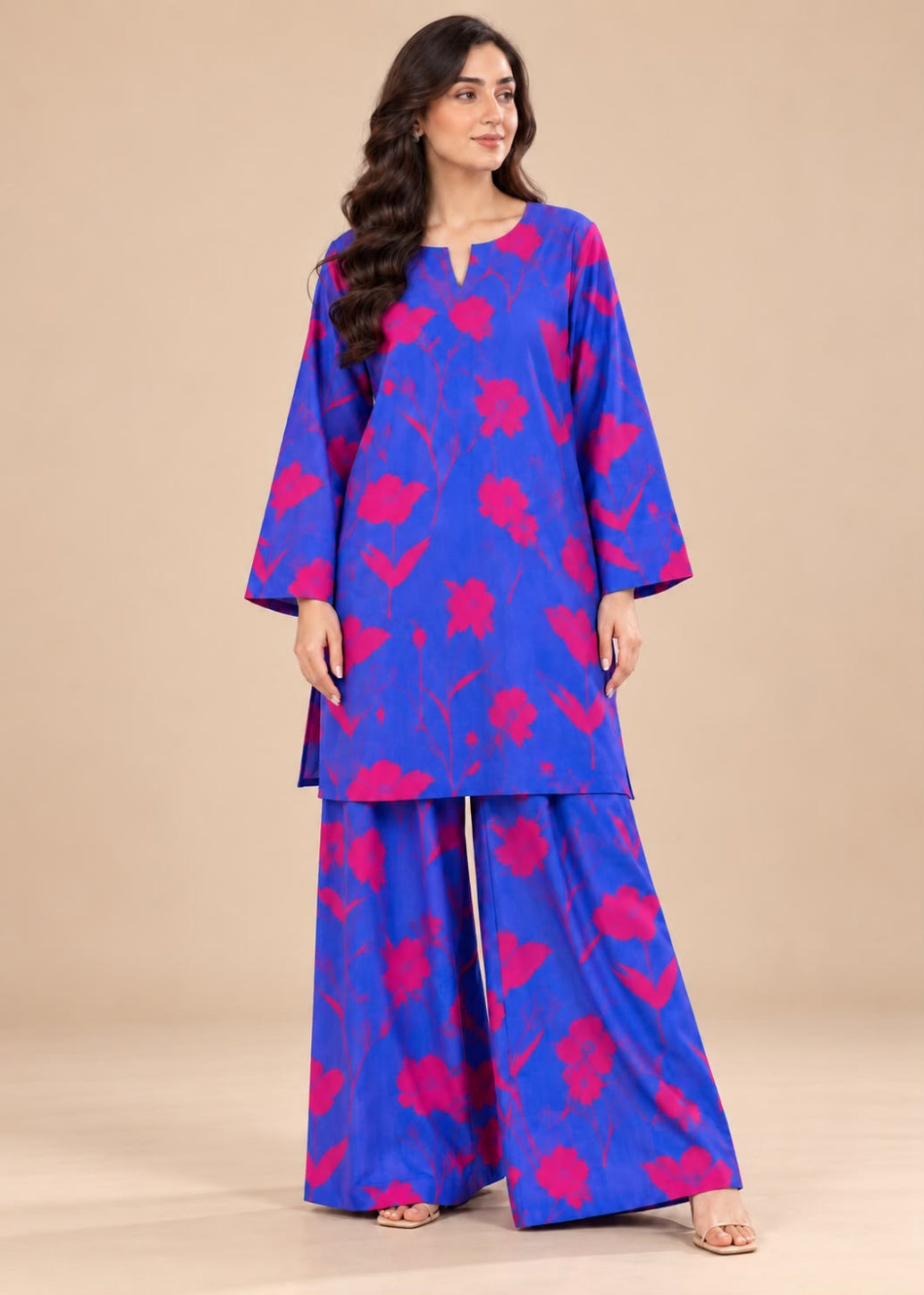 A woman modeling a vibrant royal blue two-piece kurta set with a hot pink abstract floral pattern, set against a solid beige studio background.