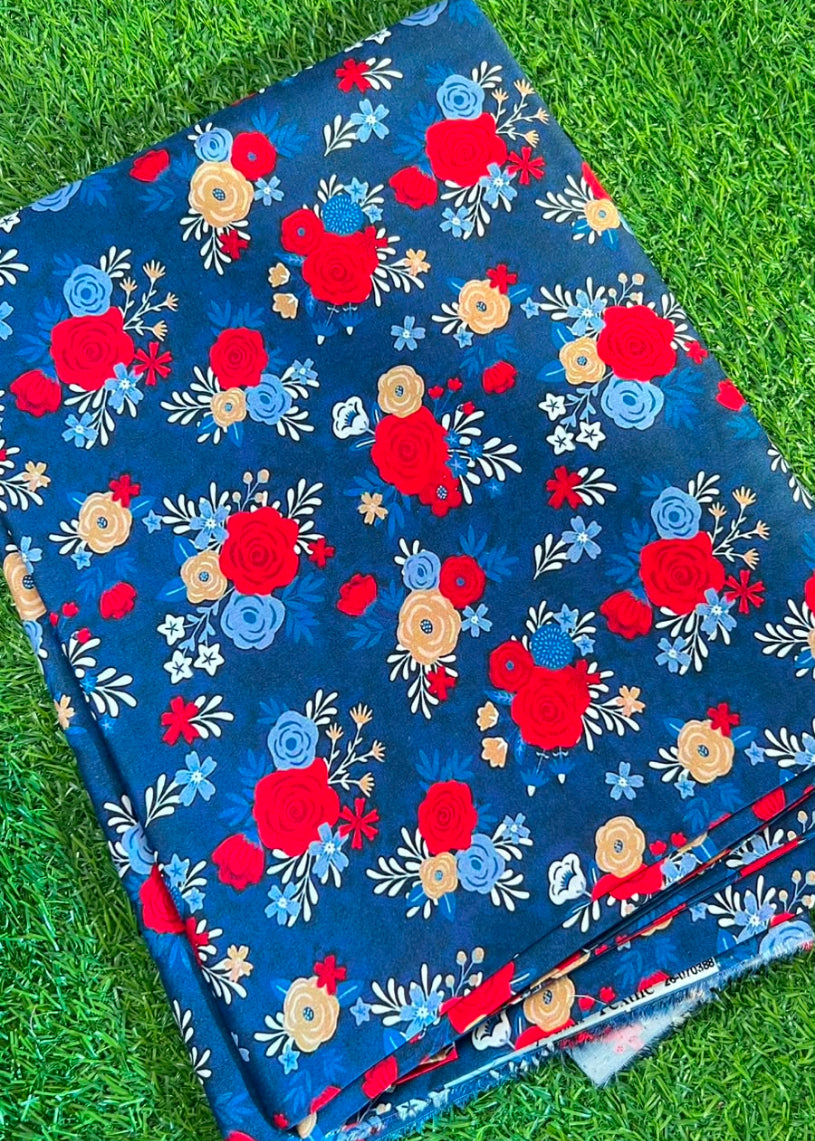 A folded piece of dark blue fabric with a vibrant red, yellow, and light blue floral pattern, laid flat on green grass.