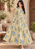 A woman models a long-sleeved, floor-length A-line dress with a blue floral print on a light olive green and white checkered base, set against an outdoor courtyard backdrop.