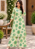 A woman models a light green and green floral print two-piece kurta set in an outdoor patio setting with plants and wooden furniture.