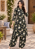 A woman models a black three-piece floral print kurta set with matching wide-leg pants and a small white handbag, standing in a sunlit outdoor courtyard setting.