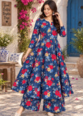 A woman models a three-piece navy blue floral kurta set with matching wide-leg pants and a long-sleeve top, set against a Mediterranean-style courtyard backdrop with a blue door and pink flowers.