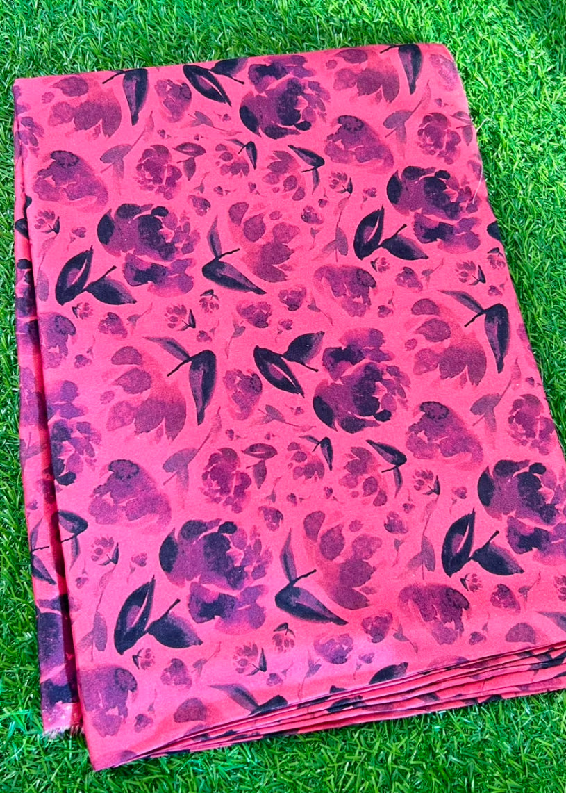A folded pink fabric with a dark purple floral pattern, laid flat on a green grass background.