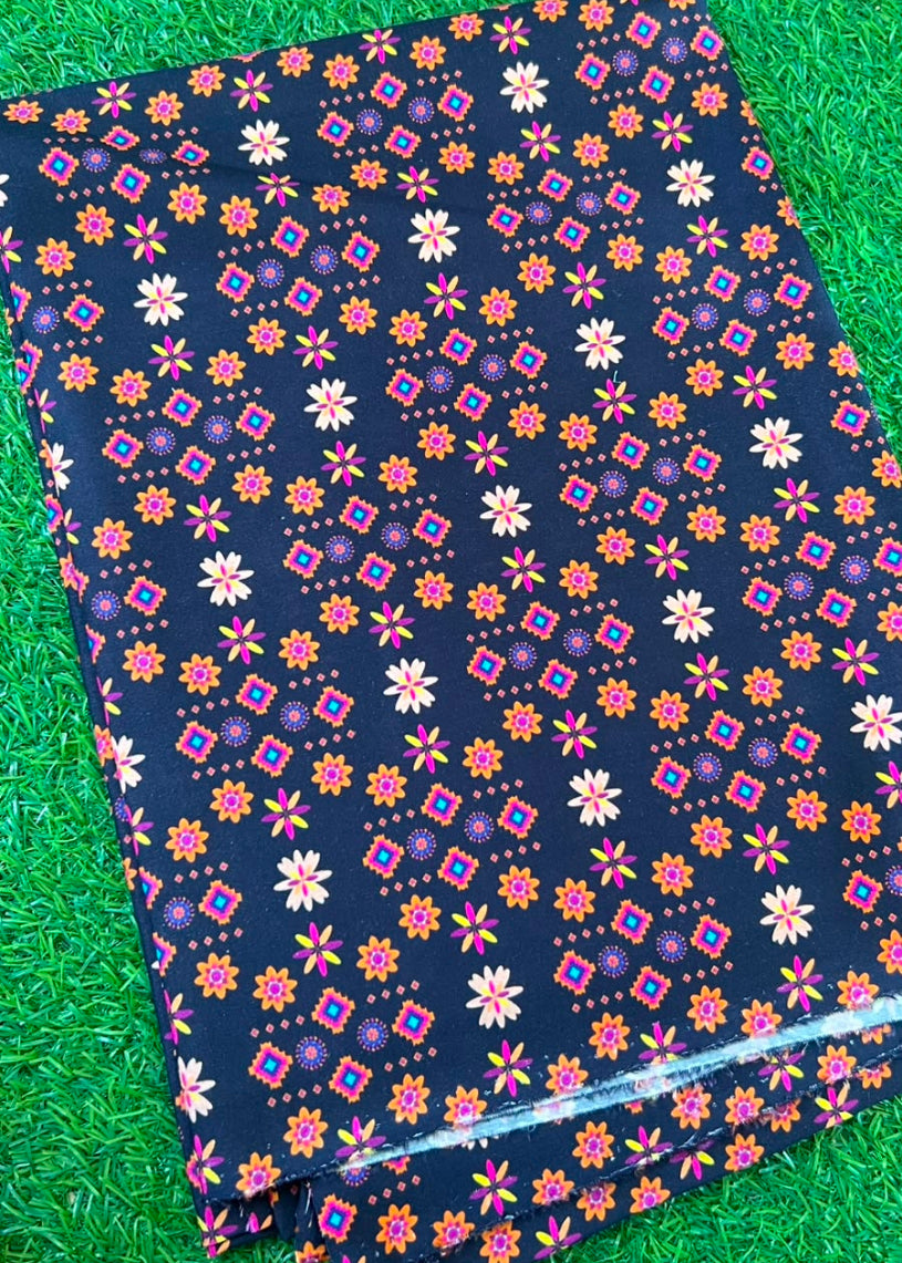 A folded piece of black fabric with a colorful geometric and floral pattern, laid flat on a green grass-like surface.