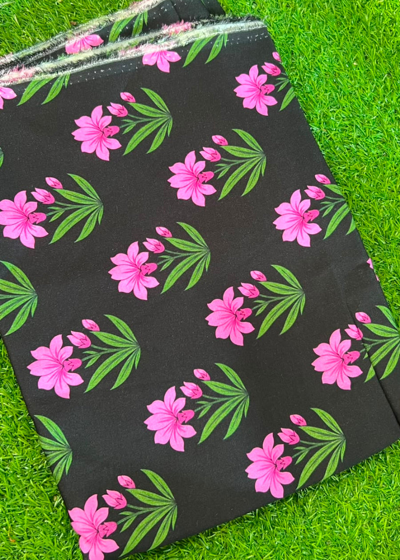 Black fabric with a repeating pattern of pink flowers and green leaves, folded and laid flat on a green grass background.