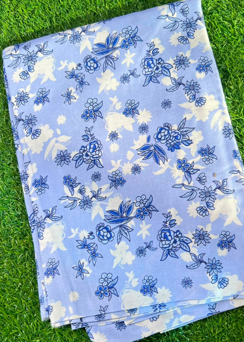 A folded piece of light blue fabric with a blue and white floral print, laid flat on a green grass background.