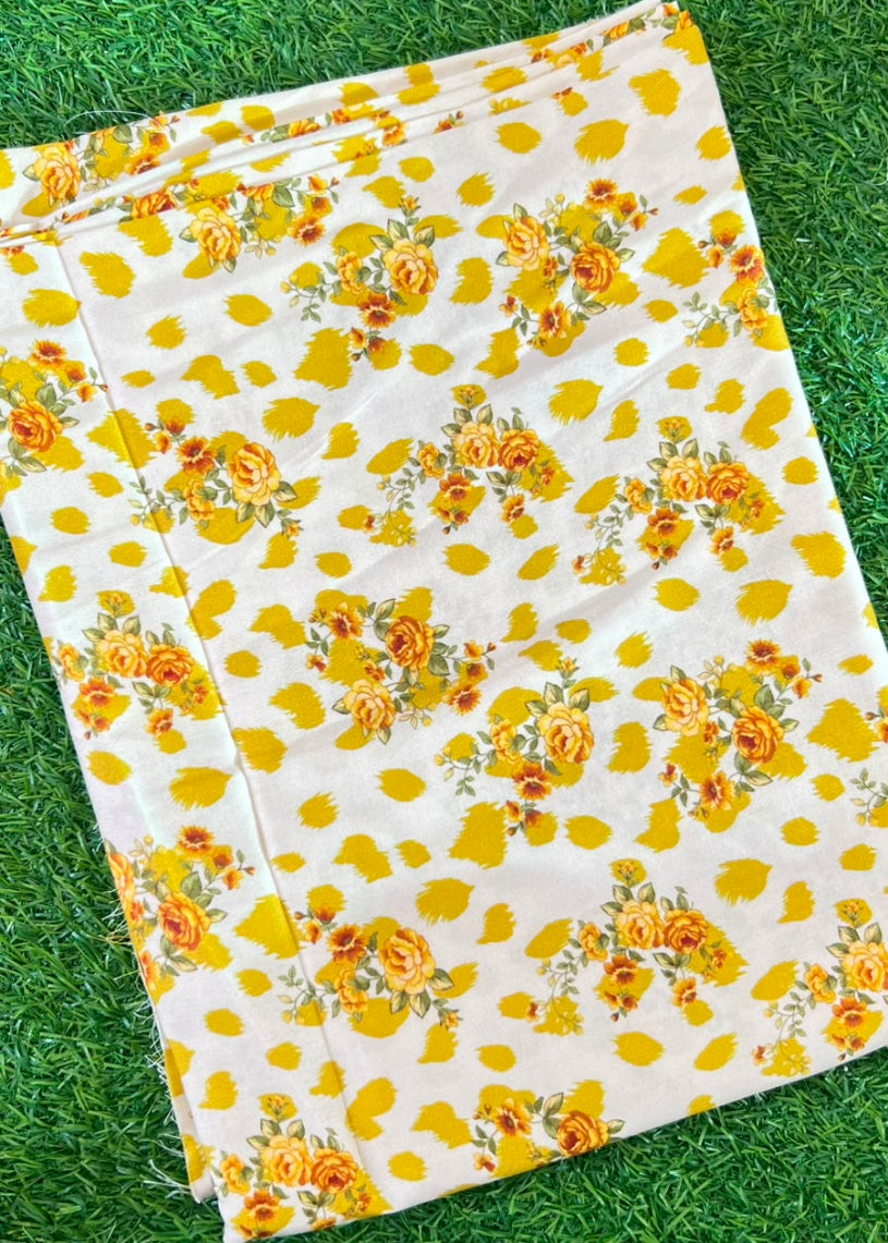 A folded white fabric item, likely a blanket or sheet, featuring a yellow rose floral pattern, laid flat on green grass.