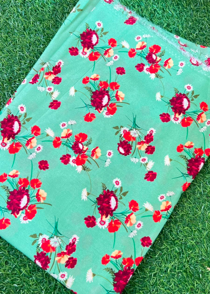 A folded mint green fabric with a vibrant red, pink, and white floral print, laid flat on a green grass background.