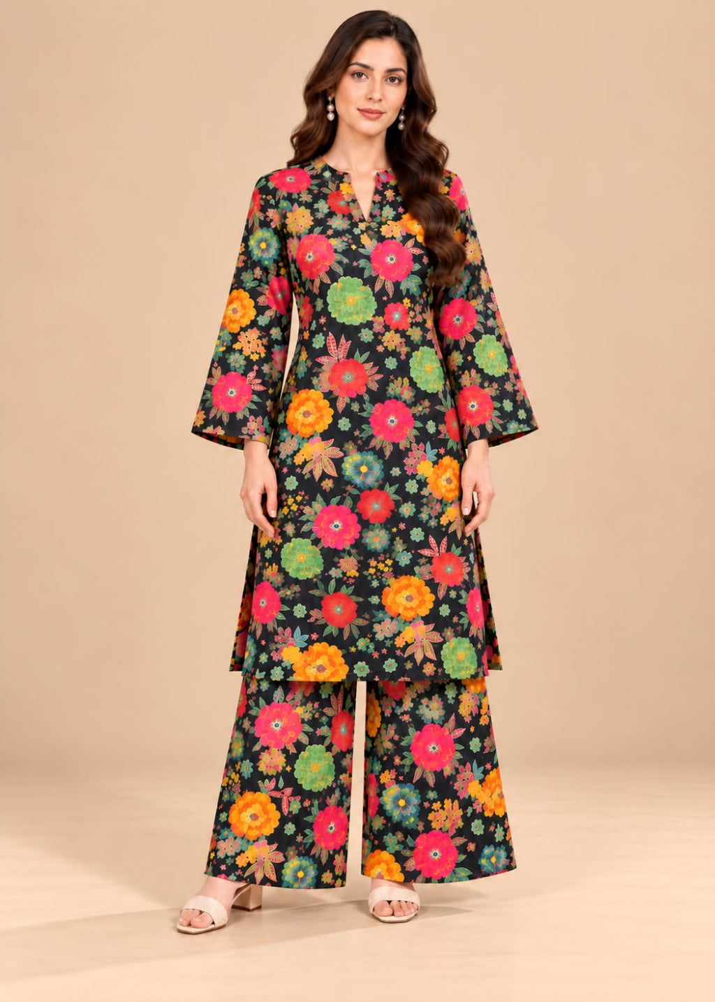 A woman modeling a black three-piece floral print kurta set with wide-leg pants, featuring colorful flowers in pink, orange, yellow, and green on a beige studio background.