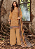 A woman models a traditional three-piece salwar kameez suit in a rustic outdoor setting with a window and tree roots. The suit features a mustard yellow kurta with intricate geometric patterns, matching wide-leg trousers, and a dupatta with a detailed border.