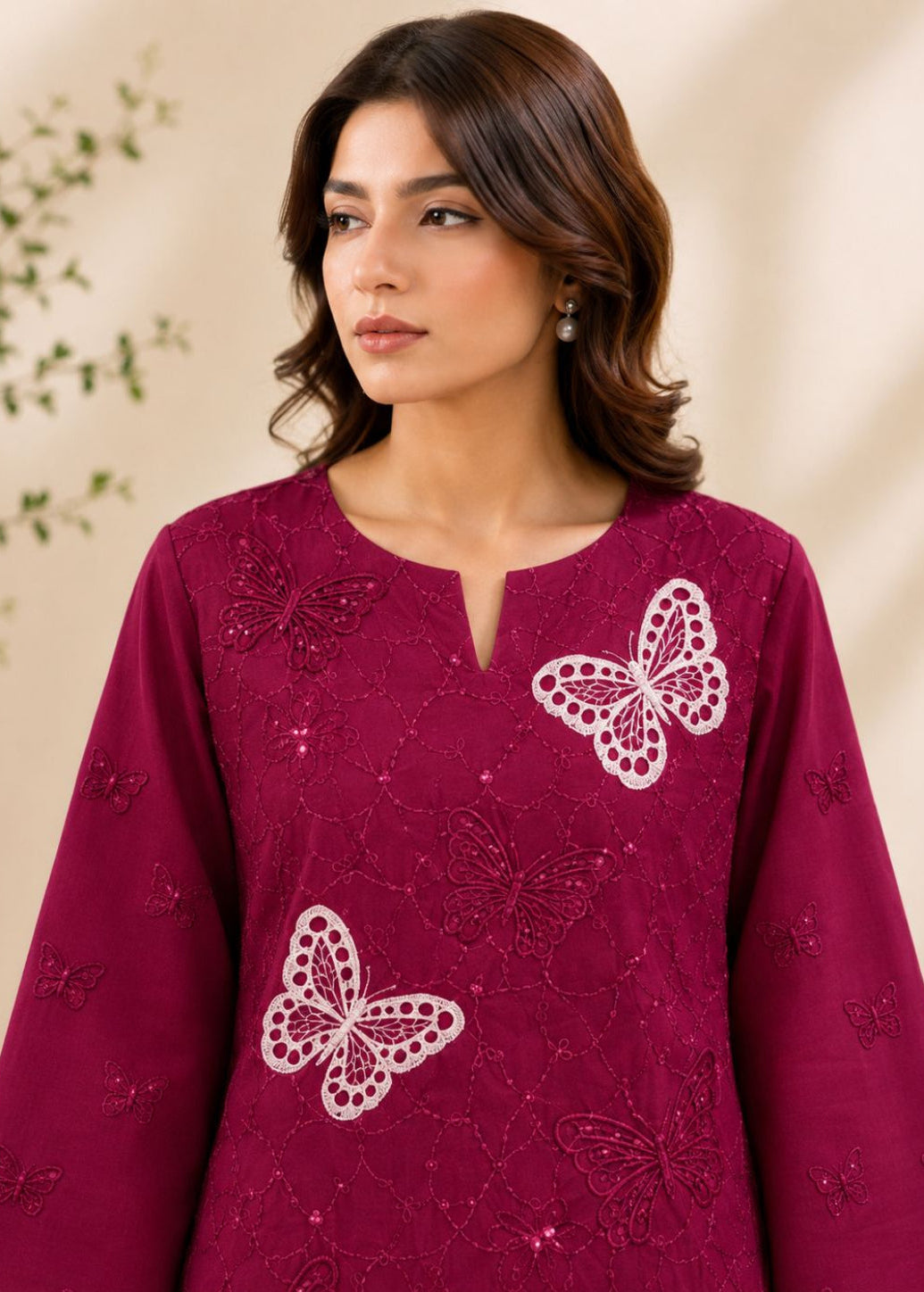 A woman wearing a deep magenta long-sleeve kurta with white embroidered butterfly motifs, photographed against a soft beige background with subtle leaf shadows.