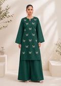 A woman modeling a dark green kurta and wide-leg pants set with embroidered butterfly motifs, set against a warm beige background with soft leaf shadows.