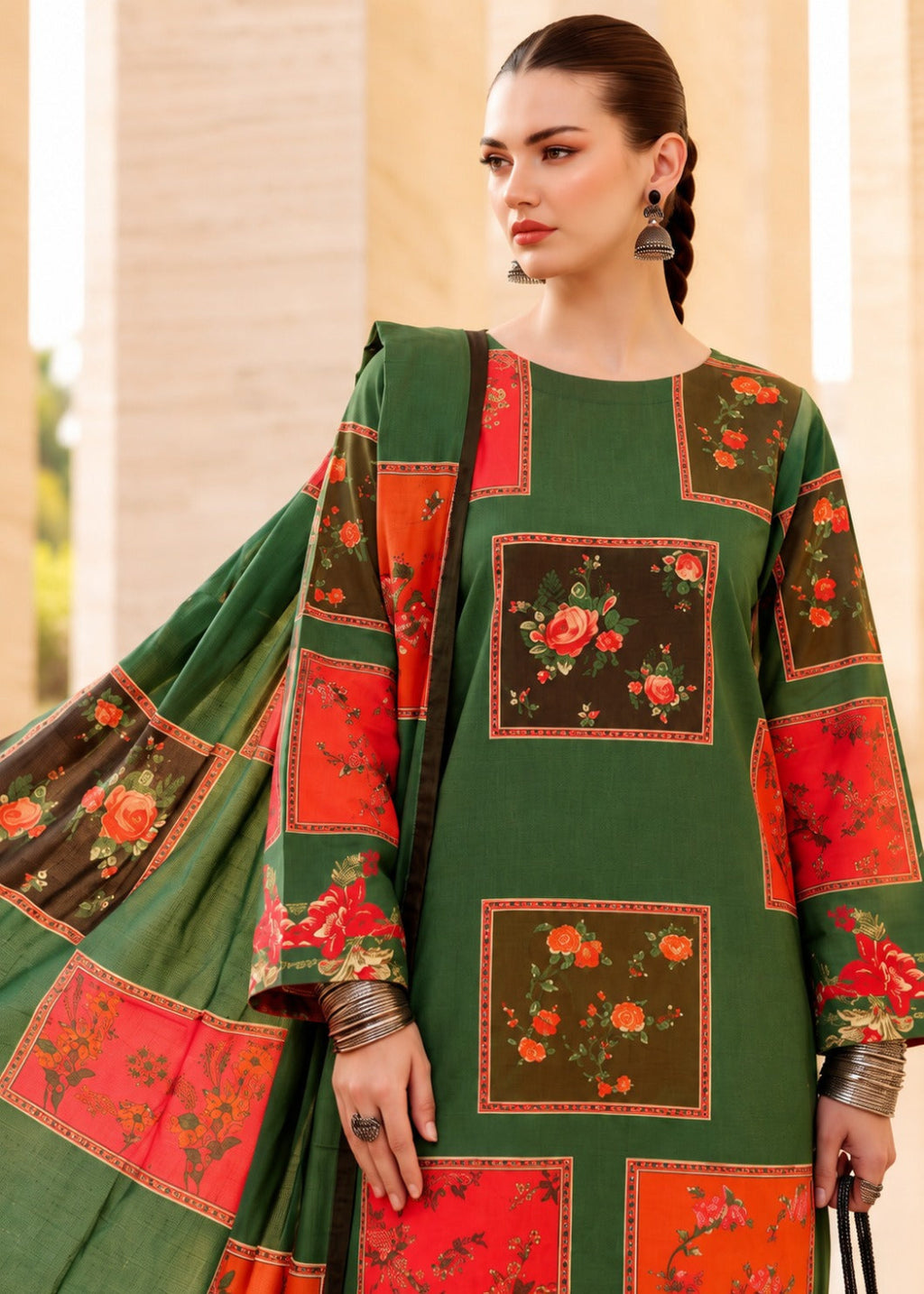 A woman models a green salwar kameez suit with red and orange floral patchwork panels and a matching dupatta, set against a warm beige architectural background.
