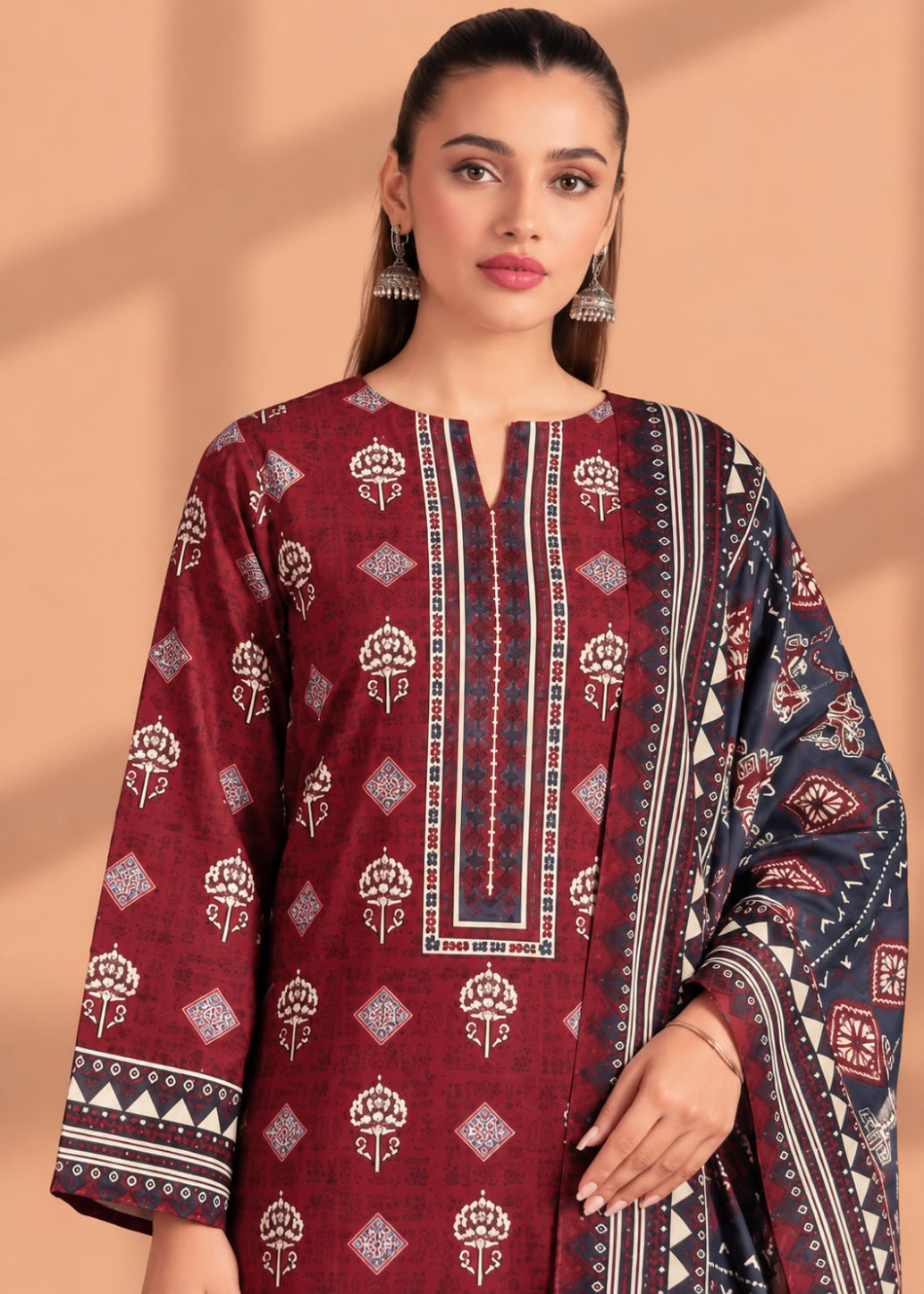 A woman modeling a traditional three-piece salwar kameez suit in maroon, navy blue, and white. The kurta features a maroon base with white block prints and a central vertical panel with geometric borders.