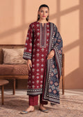 A woman models a traditional South Asian salwar kameez suit set in a warm-toned indoor setting. The set features a deep maroon kurta with intricate white and gold geometric patterns, matching maroon trousers, and a navy blue dupatta with detailed multicolor borders and motifs.