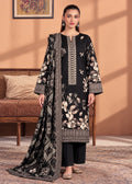 A woman models a black three-piece ethnic suit set featuring a long kurta with beige and white floral embroidery, black trousers, and a matching printed dupatta, set against a warm peach-colored indoor background.