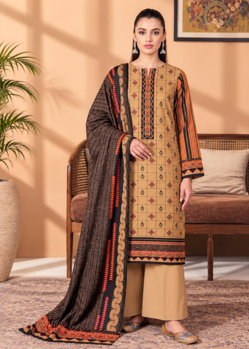 A woman models a traditional South Asian salwar kameez suit set in a warm indoor setting. The set features a beige kurta with geometric patterns and orange and black borders, paired with a dark brown dupatta featuring orange and red geometric motifs, and beige trousers.
