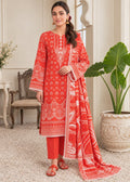 A woman models a three-piece red and white printed ethnic suit in a decorated indoor setting. The set includes a long kurta with intricate white patterns, matching red pants, and a coordinating dupatta draped over her shoulder.