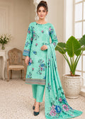 A woman models a mint green three-piece salwar kameez suit with floral embroidery, matching trousers, and a long dupatta, set against an elegant indoor background with a potted plant.