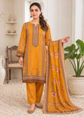 A woman models a traditional Indian salwar kameez suit in mustard yellow and brown, featuring embroidered details, paired with matching trousers and a floral printed dupatta, set in a bright, neutral indoor room.