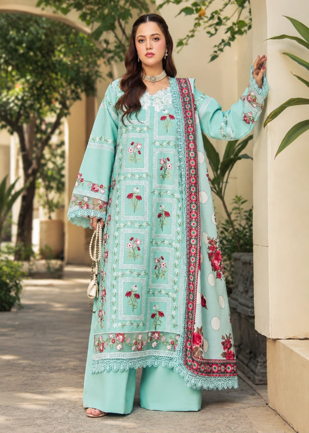 A woman models a traditional three-piece beige ethnic suit with brown floral embroidery and a matching dupatta, set against a beige wooden grid wall background.