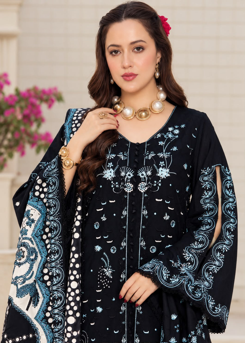 A woman models a beige traditional embroidered outfit with brown floral and geometric embroidery, featuring a matching dupatta with a black and white patterned border, set against a softly blurred indoor background.
