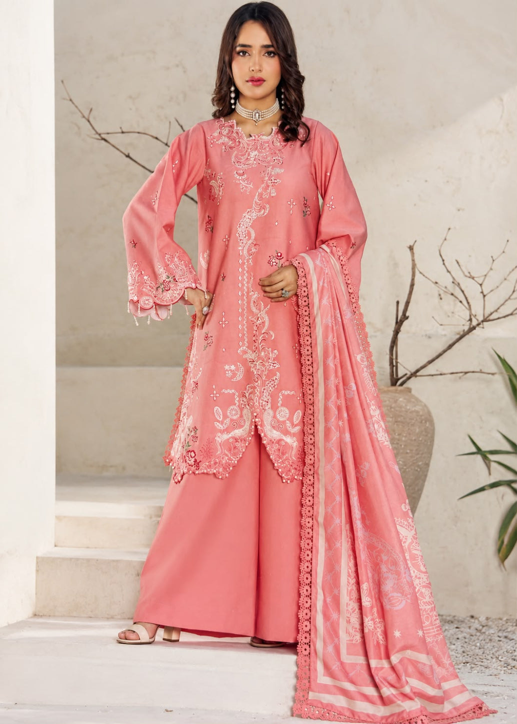 A woman models a traditional three-piece beige ethnic suit with brown floral embroidery and a matching dupatta, set against a beige wooden grid wall background.