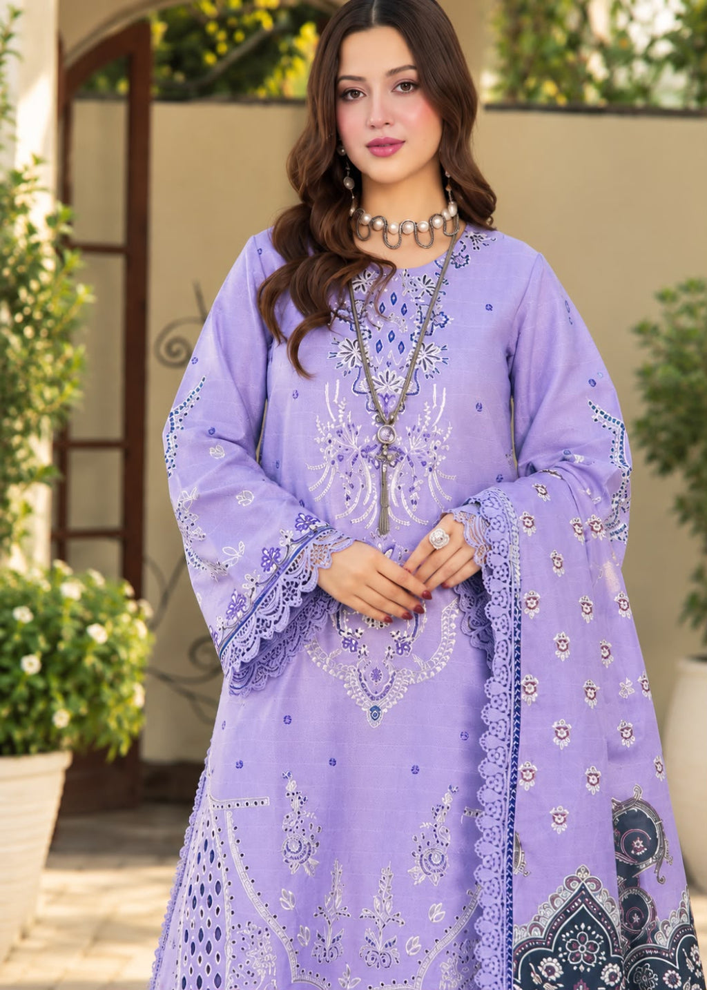 A woman models a beige traditional embroidered outfit with brown floral and geometric embroidery, featuring a matching dupatta with a black and white patterned border, set against a softly blurred indoor background.