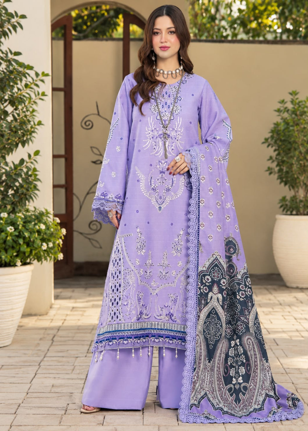 A woman models a traditional three-piece beige ethnic suit with brown floral embroidery and a matching dupatta, set against a beige wooden grid wall background.