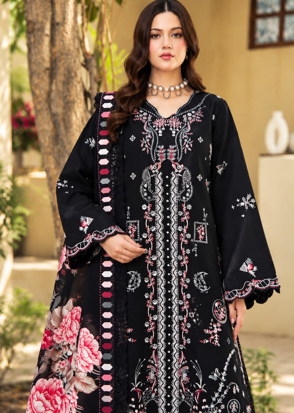 A woman models a beige traditional embroidered outfit with brown floral and geometric embroidery, featuring a matching dupatta with a black and white patterned border, set against a softly blurred indoor background.