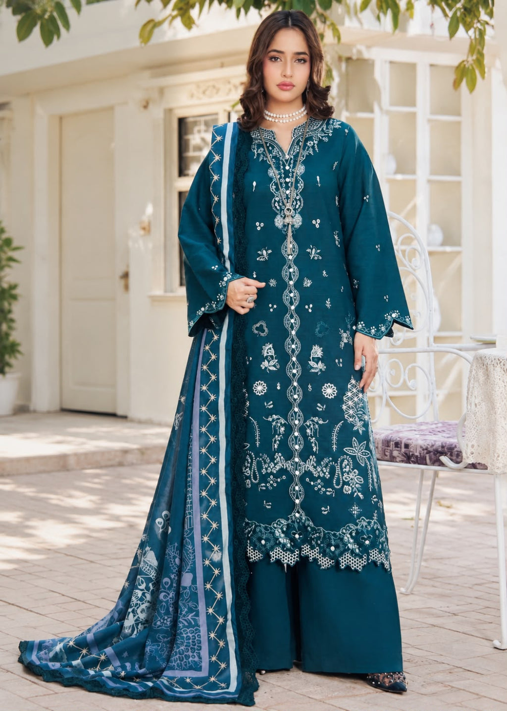 A woman models a traditional three-piece beige ethnic suit with brown floral embroidery and a matching dupatta, set against a beige wooden grid wall background.