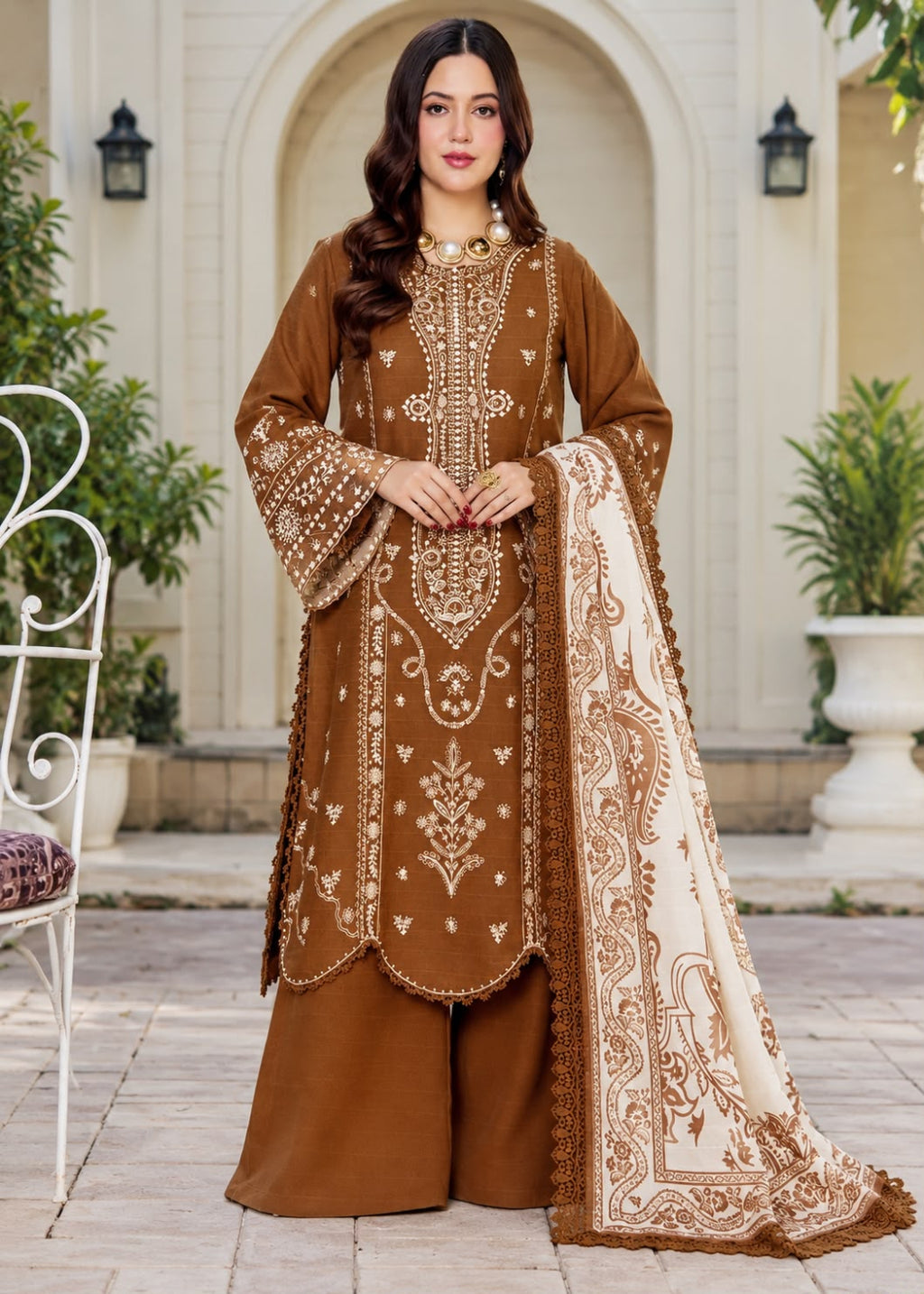 A woman models a traditional three-piece beige ethnic suit with brown floral embroidery and a matching dupatta, set against a beige wooden grid wall background.
